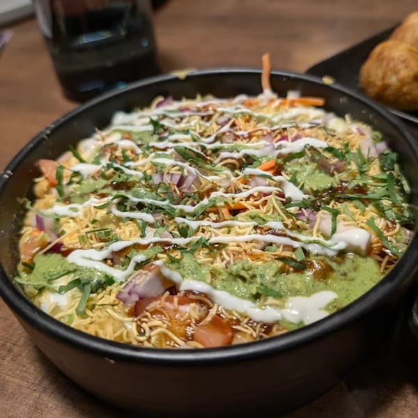 A close-up of a colorful Asian-fusion dish topped with sauces, onions, and crispy noodles.