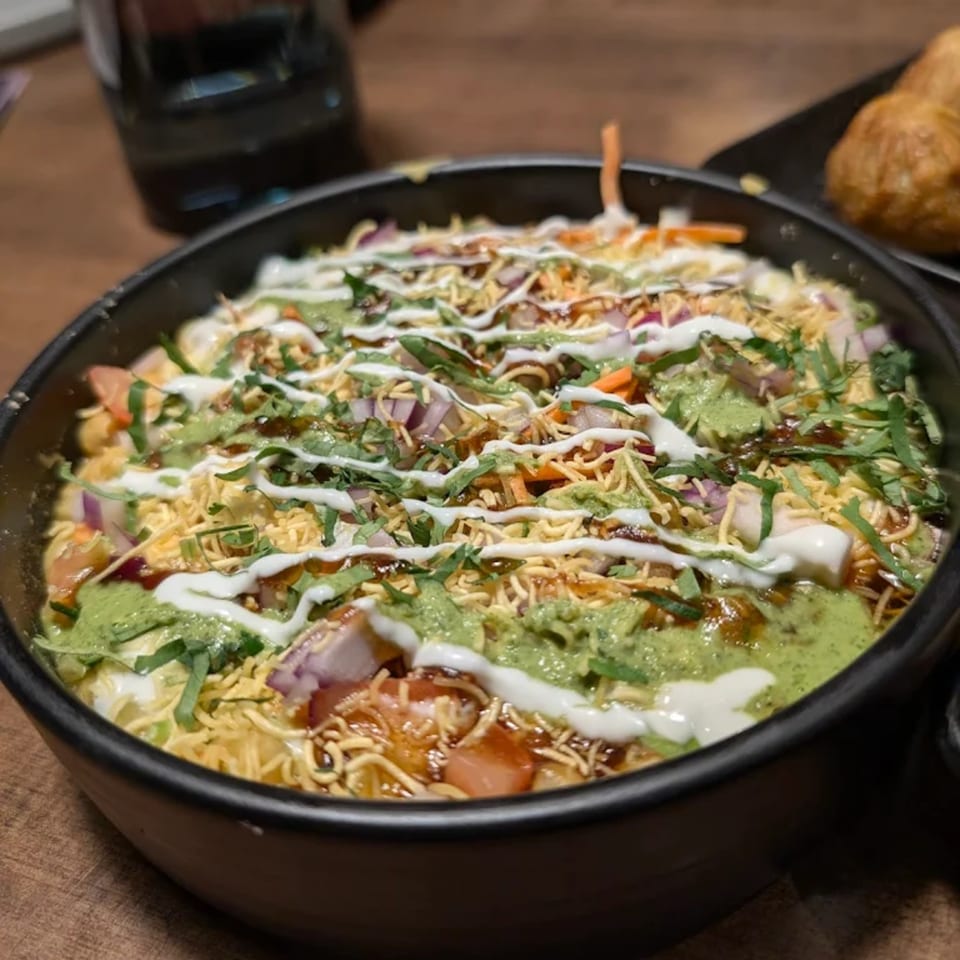 A close-up of a colorful Asian-fusion dish topped with sauces, onions, and crispy noodles.