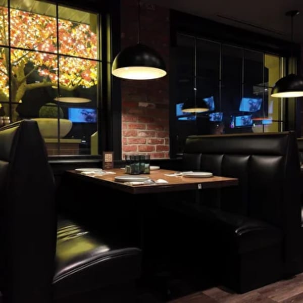 Cozy Amrut Fusion dining area with dark booths, wooden tables, and a window view of illuminated trees.