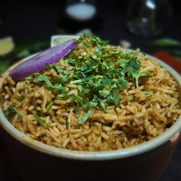Amrut Fusion's Asian-fusion rice dish, garnished with fresh cilantro and a slice of red onion.