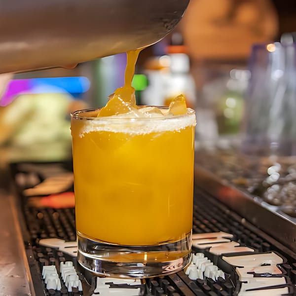 A bartender pours a vibrant orange cocktail with a salted rim into a glass at Amrut Fusion.
