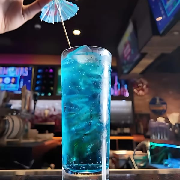 A vibrant blue cocktail with ice and a small umbrella, set against a blurred bar background.