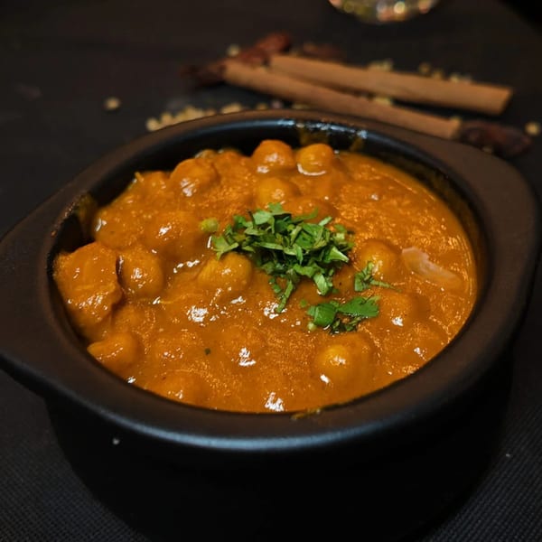 A black bowl of Amrut Fusion's chickpea curry, garnished with fresh cilantro, on a dark surface.