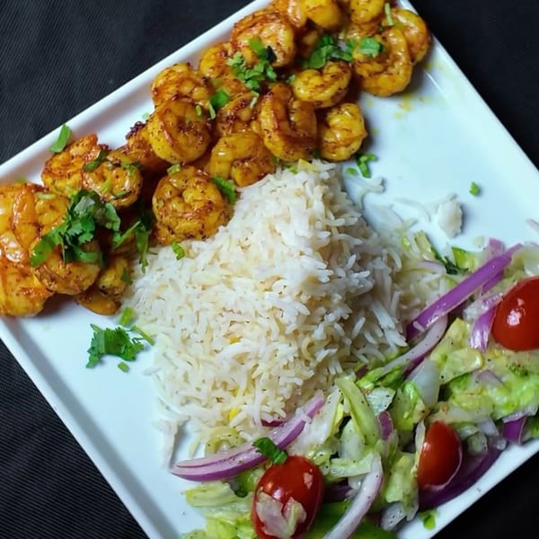 A white rectangular plate holds golden shrimp, white rice, and a fresh salad with cherry tomatoes and red onion.