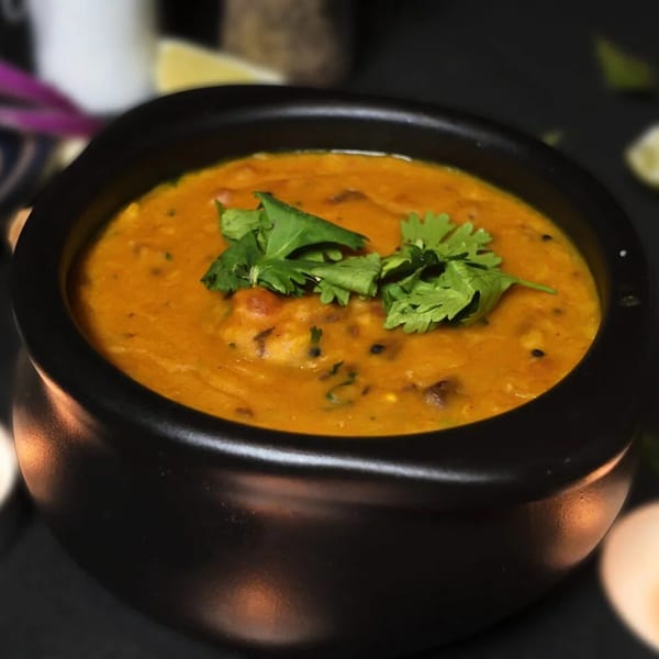 A black bowl of Amrut Fusion's orange-colored dal, garnished with fresh green cilantro.