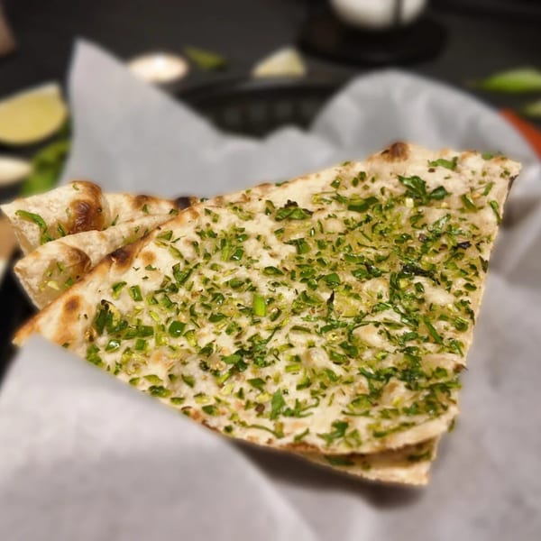 Close-up of garlic naan bread topped with fresh green herbs, served in a white paper-lined basket.
