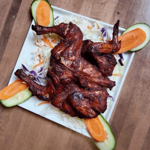 Whole roasted chicken, garnished with shredded cabbage, carrots, and cucumber slices on a white plate.