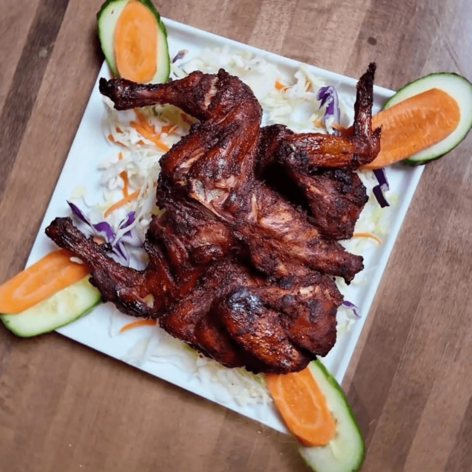 Whole roasted chicken, garnished with shredded cabbage, carrots, and cucumber slices on a white plate.