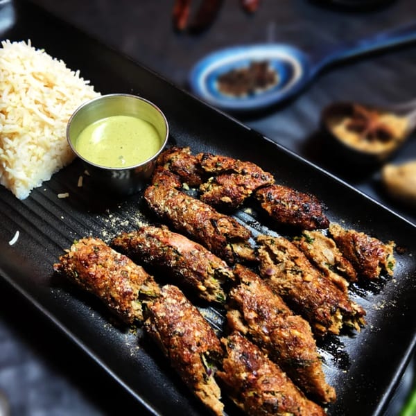 Amrut Fusion's Asian-fusion seekh kebabs with rice and green chutney on a black platter.