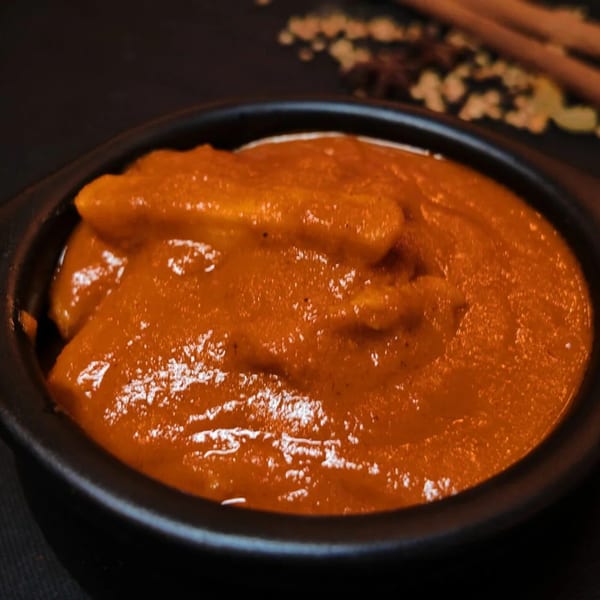Close-up of a dark bowl filled with a rich, orange-red Asian-fusion curry, with spices in the background.