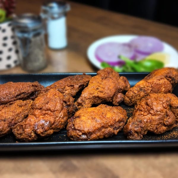 A black platter of crispy, spice-dusted chicken wings with a side of sliced red onions and lime.