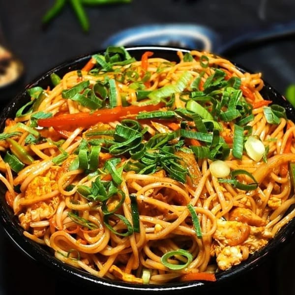 Close-up of Amrut Fusion's Asian-fusion noodles with vegetables and scallions in a black bowl.