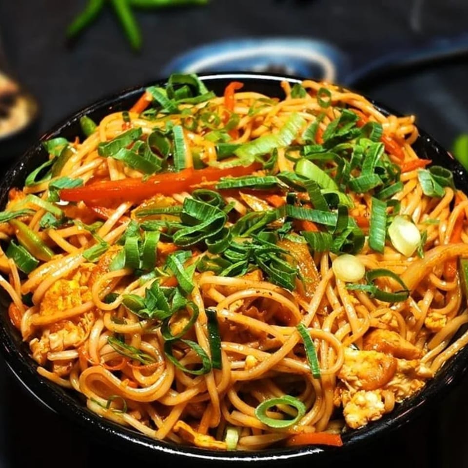 Close-up of Amrut Fusion's Asian-fusion noodles with vegetables and scallions in a black bowl.