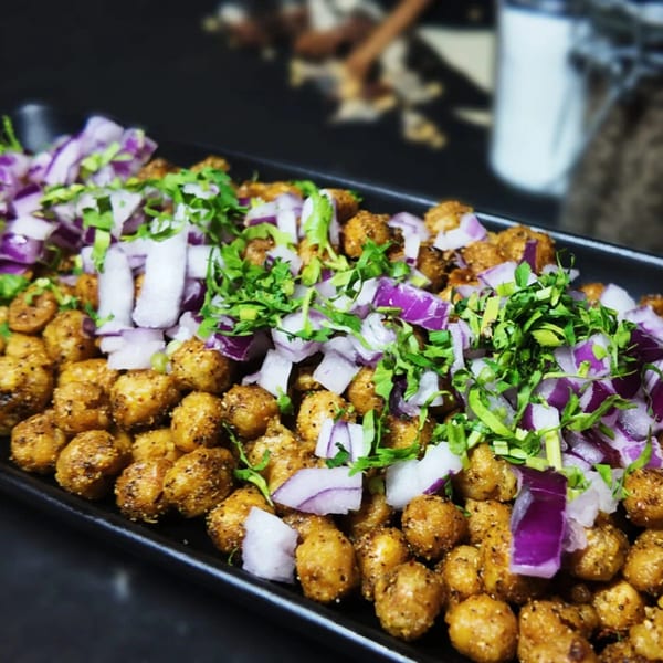 Close-up of golden-brown chickpeas topped with diced red onions and fresh green cilantro on a black platter.