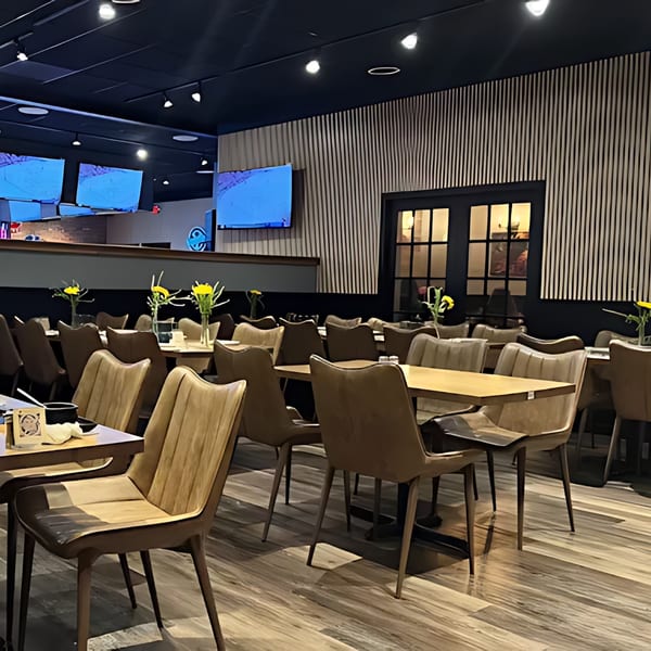 Interior of Amrut Fusion dining room with tables, chairs, wood paneling, and TVs.