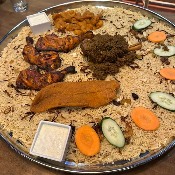 A large platter of Amrut Fusion's Asian-fusion rice, chicken, fish, and beef with cucumber and carrot slices.