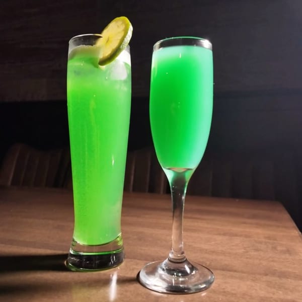 Two vibrant green cocktails, one garnished with a lime slice, sit on a wooden table.